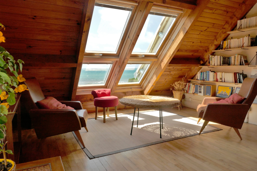 Le salon avec parquet en bois, vue sur la mer et bibliothèque dans le gîte Ti Bili en Bretagne